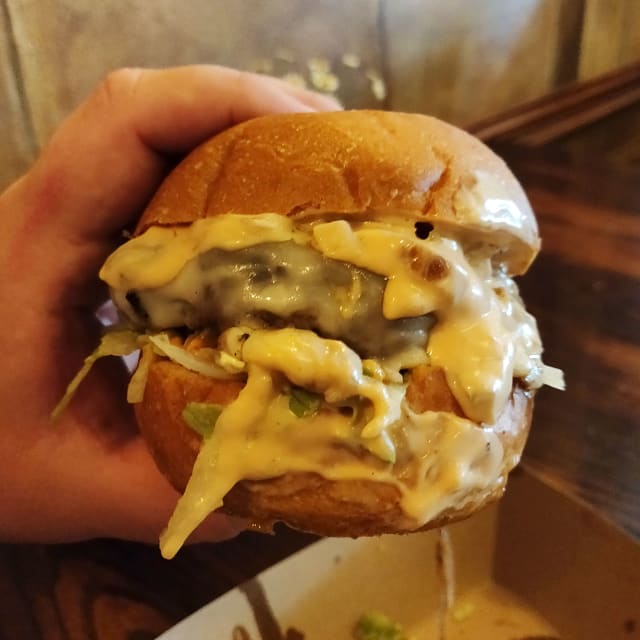 Hand holding a burger with a charred patty, creamy sauce, and shredded lettuce, highlighting the unique flavors from Ya Hala's Burger Week offering.